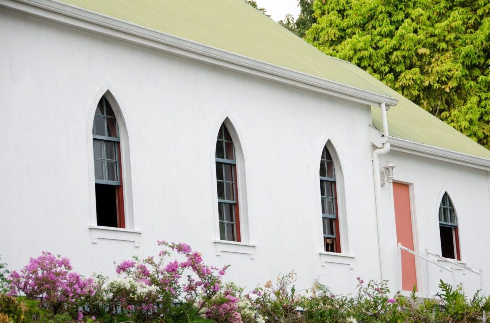 A church with three windows and flowers in front of it.