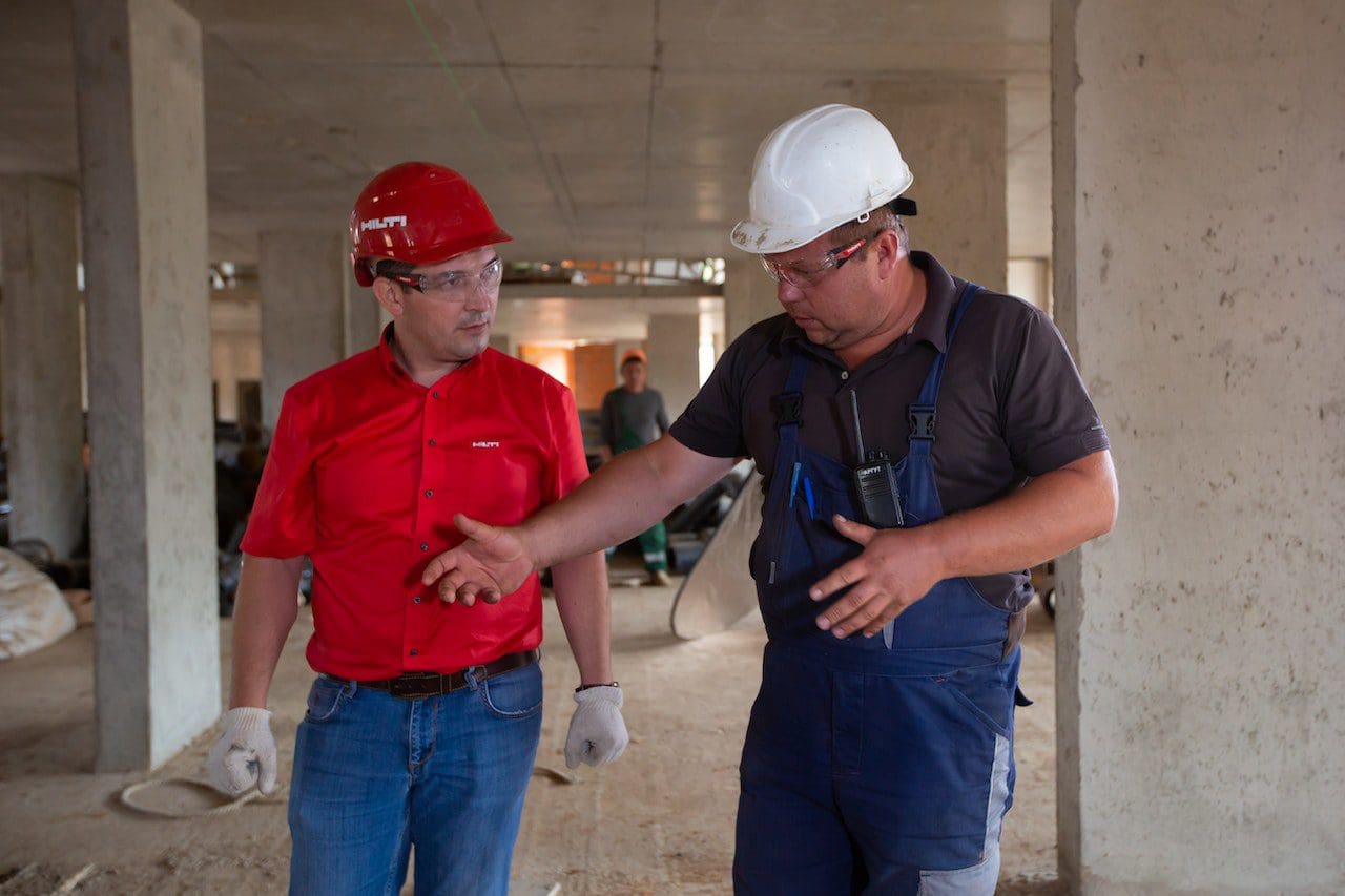 Two men in hard hats and gloves talking to each other.