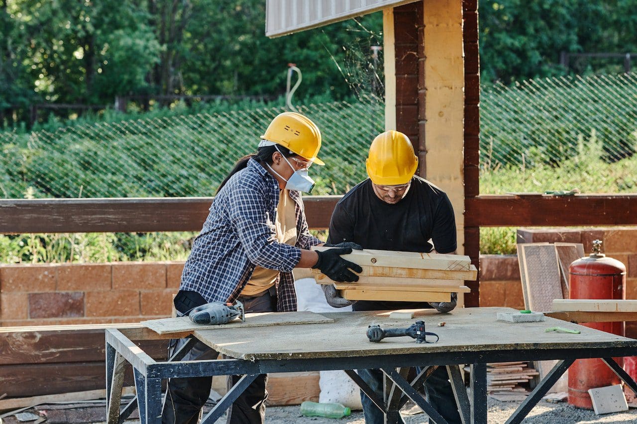 Two men wearing hard hats and gloves working on a table.