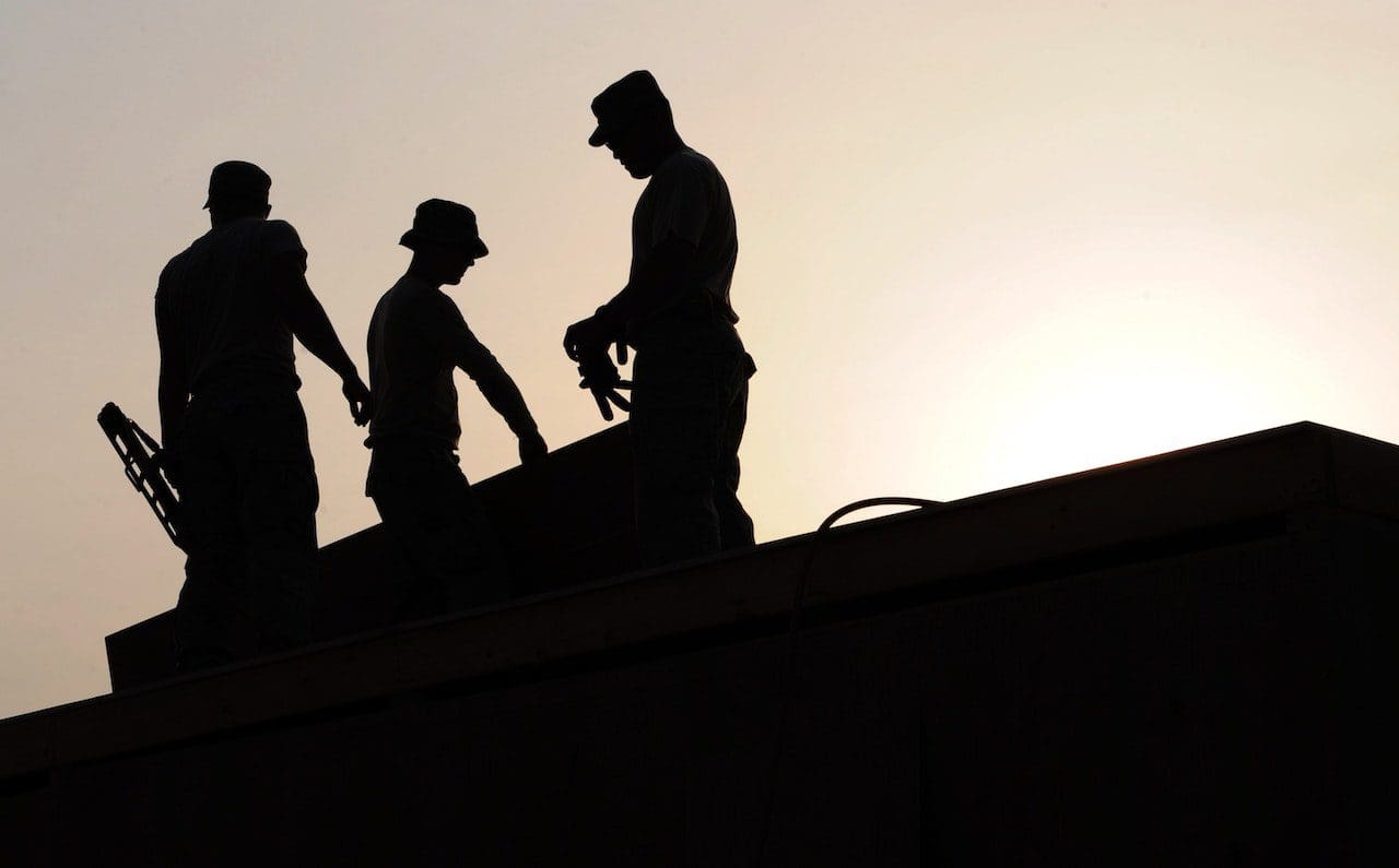 Three men are working on a building at sunset.