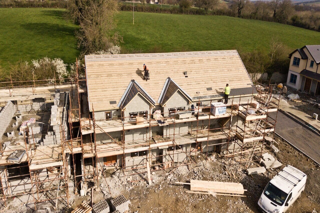 A construction site with workers working on the roof of a house.