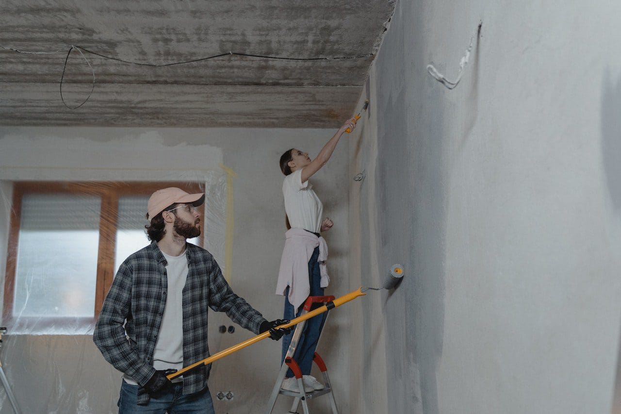 Two men are working on a wall in the house.